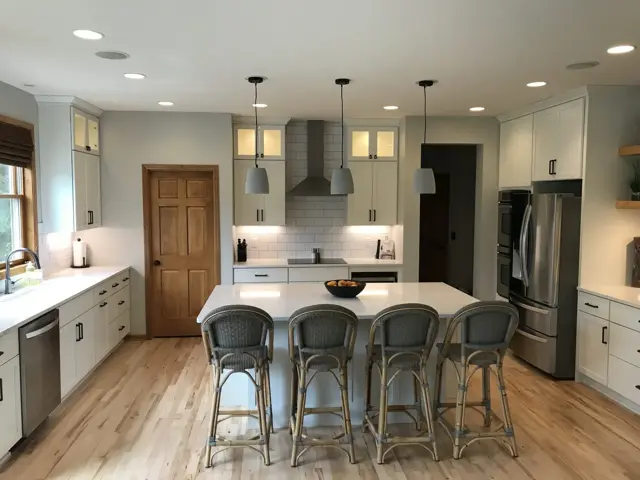 Rebuilt Chanhassen kitchen with white cabinets, a large island with rattan stools, and a stainless range hood after water damage restoration by Ungerman