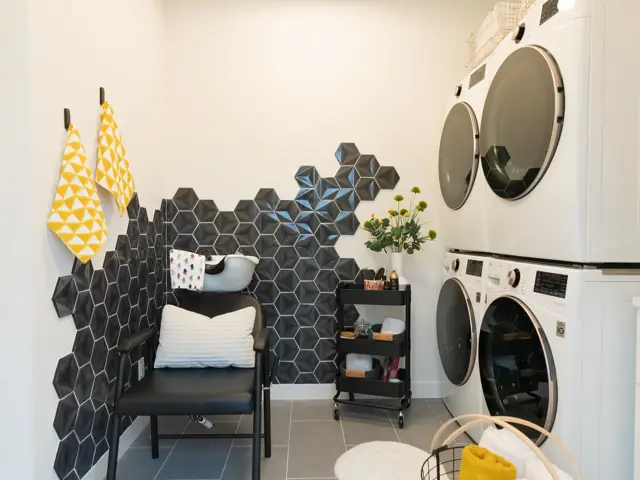Rebuilt contemporary laundry room with white stacking washers and dryers and a black geometric-tile feature wall after dryer fire restoration by Ungerman