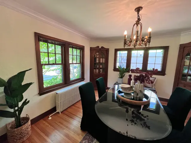 Restored 1920s dining room with refinished hardwood floors, a period column radiator under the windows, and leaded-glass built-in cabinets after frozen pipe and radiator water damage restoration by Ungerman