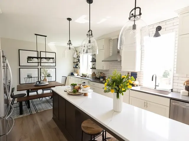 Modern farmhouse kitchen rebuilt with a waterfall-quartz island, glass pendant lights, and a vented hood after a lightning-strike fire, opening to a new dining room