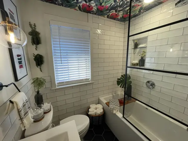 Remodeled 1940s Minneapolis bathroom with white subway tile, a black-framed glass tub shower, a tiled niche, and a floral wallpaper ceiling after a whole-home remodel by Ungerman