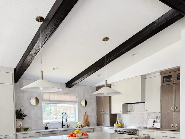 Rebuilt Plymouth kitchen with a large island, rattan stools, and exposed beams under a vaulted ceiling after water damage restoration by Ungerman