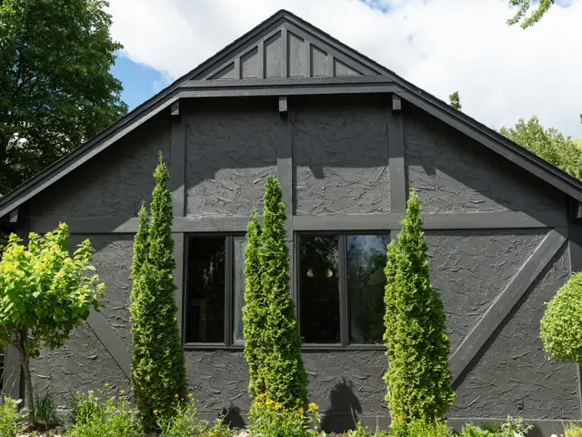 Charcoal tudor-style gable with new roof shingles and columnar arborvitae after storm roof replacement and an exterior repaint by Ungerman