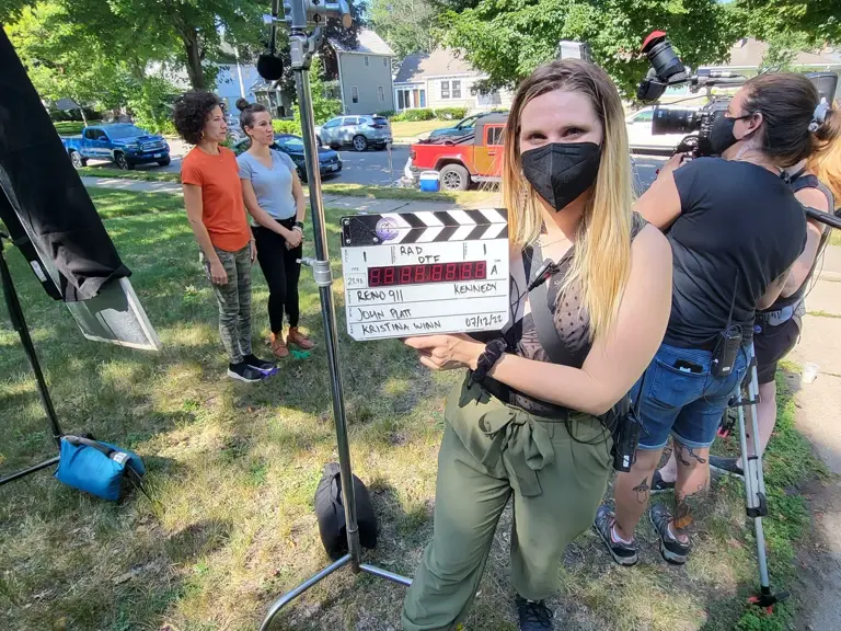 A crew member holds a clapperboard in front of the camera on the driveway of a home before a take