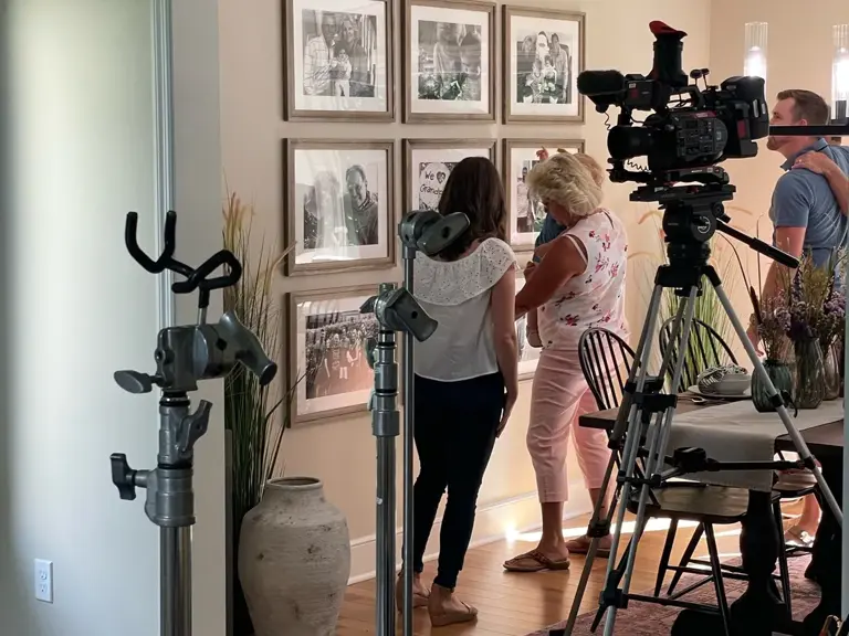 Camera and lighting set up inside a finished living room with a gallery wall of framed photographs
