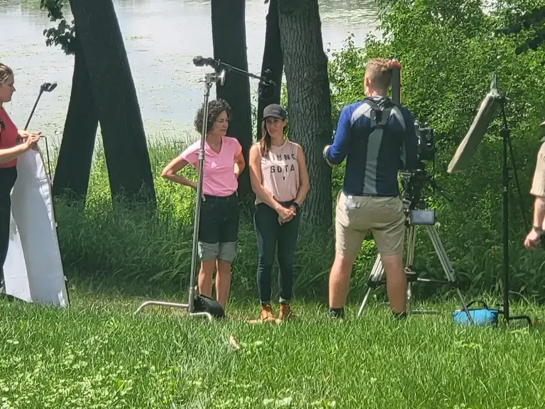 Production crew with a boom pole and reflector filming a group beside a lake