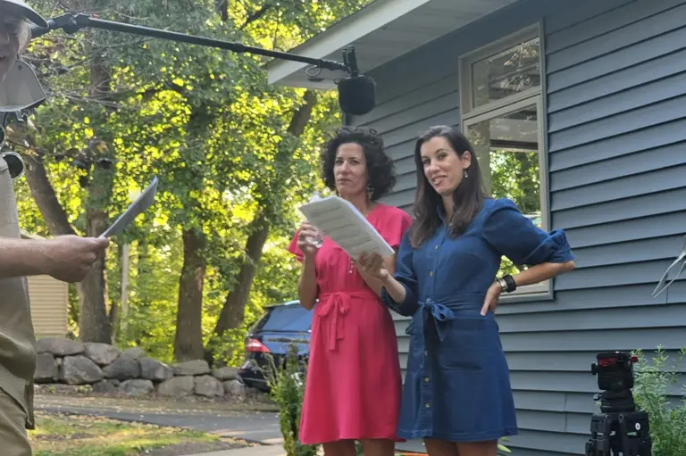 An HGTV production crew with a boom microphone films two people outside a Twin Cities home