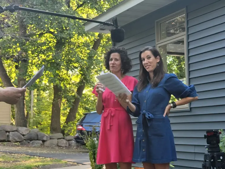 An HGTV production crew with a boom microphone films two people outside a Twin Cities home