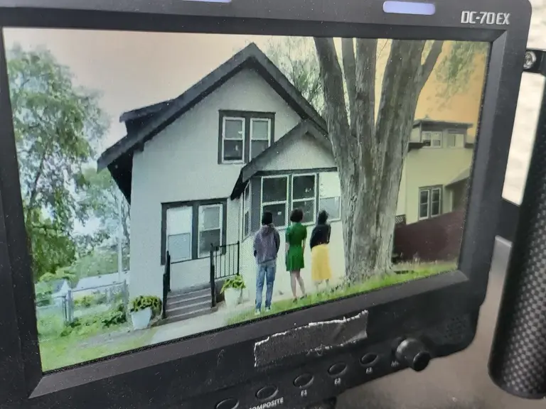 A director monitor showing the front of a house with two people on the porch during filming