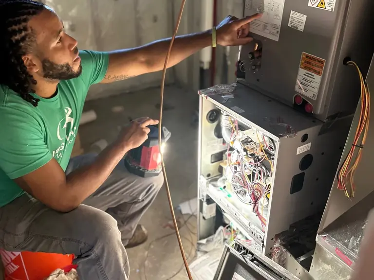 An Ungerman technician checking the wiring diagram on an open furnace control panel during a heating service call
