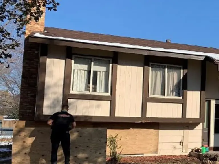 Split-level home with the lower level sheeted over in plywood beside the chimney after a vehicle broke through the exterior wall