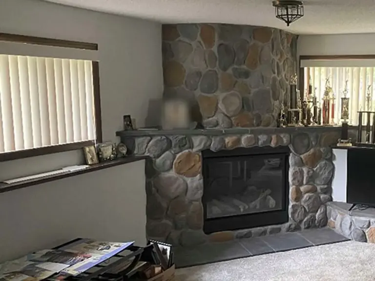 The same living room rebuilt with a river rock fireplace, a glass-front gas insert, a tile hearth, and the window restored where the wall was breached