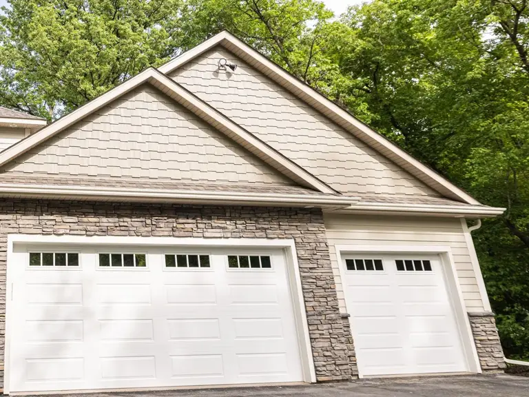 Restored garage exterior with new cedar shake gable, stone veneer, siding, and white overhead doors after fire restoration
