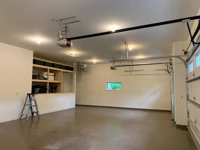 Rebuilt garage with finished walls and ceiling, sealed floor, built-in storage, and new overhead doors after fire restoration