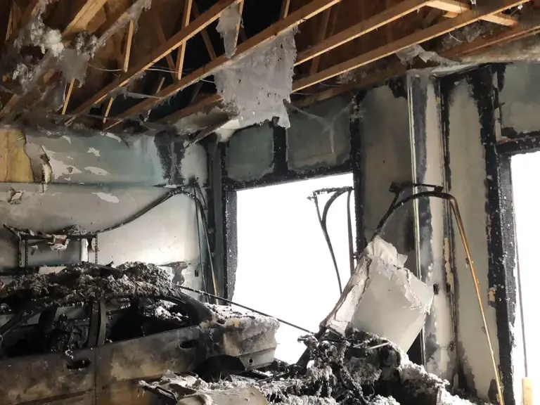 Attached garage gutted by fire, with charred roof trusses, blackened walls, and a burned-out vehicle inside