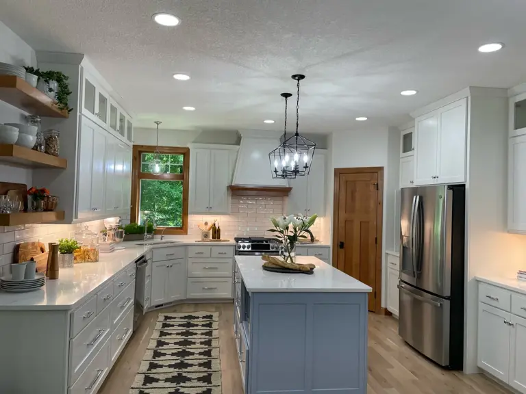 Rebuilt kitchen in the same footprint with white and grey cabinetry, quartz counters, subway tile, and a corner sink under the window