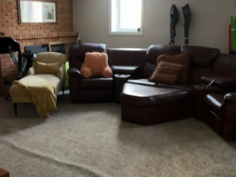 Original lower-level family room with an unpainted brick fireplace, worn carpet, and a leather sectional before restoration