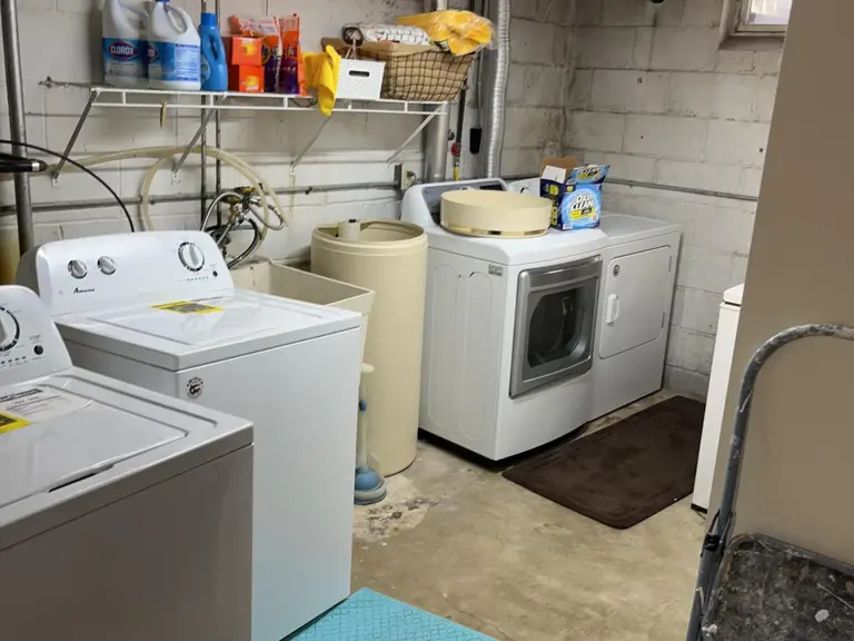 Basement laundry area on bare concrete with unpainted block walls, water softener, and wire shelving
