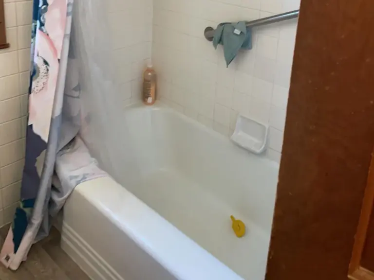 Original bathroom tub with a shower curtain and dated white square wall tile before water damage restoration