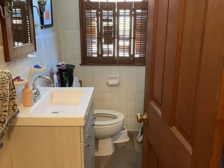 Original bathroom with a light laminate vanity, white square tile, and a wood door before restoration