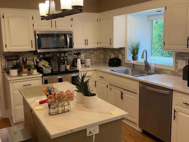 Dated Burnsville kitchen with a microwave over the range, tan stone backsplash, dark walls, and a small island after a supply-line flood