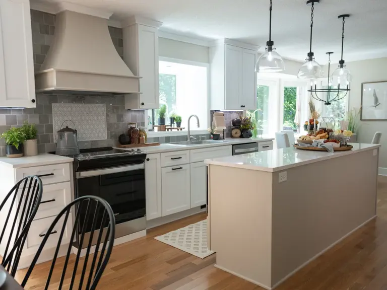 The rebuilt range wall with a custom hood, grey tile backsplash, and a glass cooktop, with black counter stools at the new island