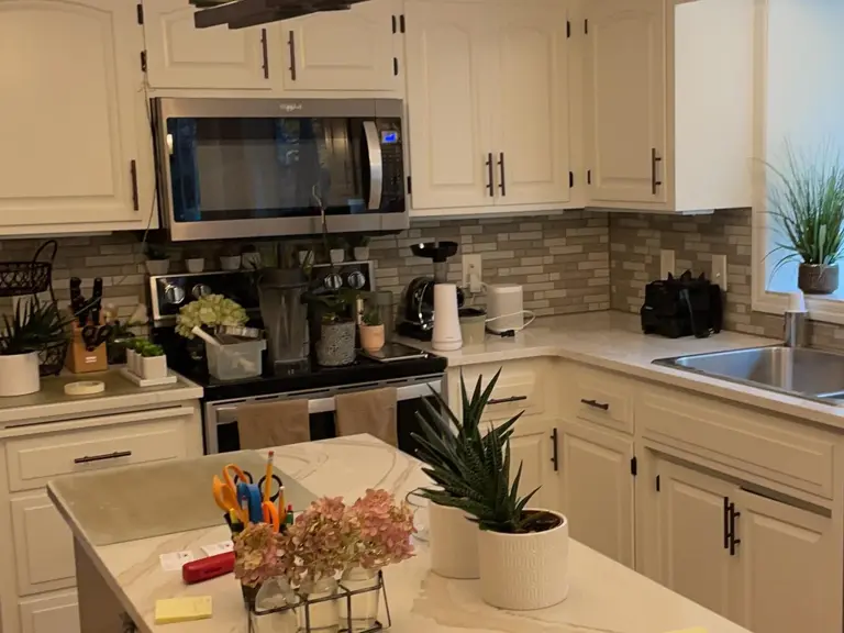 Original range wall with a stainless microwave mounted over the range and a tan stacked-stone backsplash before restoration