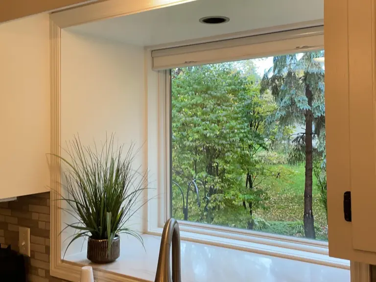 Kitchen sink below a window looking onto the wooded backyard, with a stone-tile backsplash, before restoration