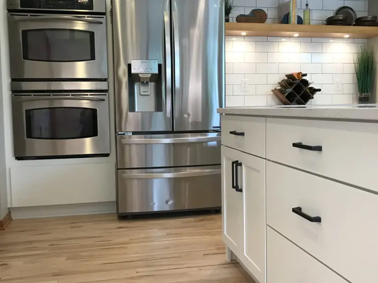 The same wall rebuilt with white cabinetry, black hardware, subway tile, and open display shelving