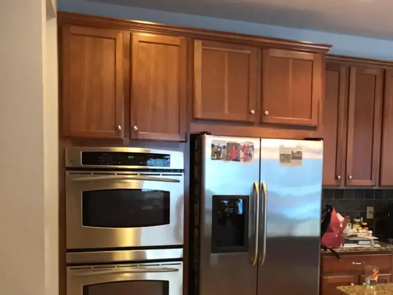 Original wall of cherry cabinets around the double ovens and refrigerator before restoration