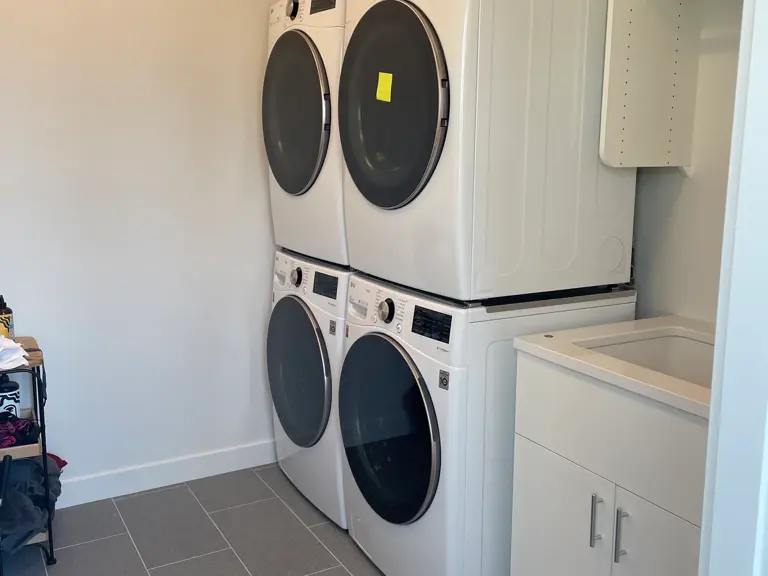 Two columns of stacked front-load washers and dryers against a plain white wall, one dryer tagged out of service after the fire