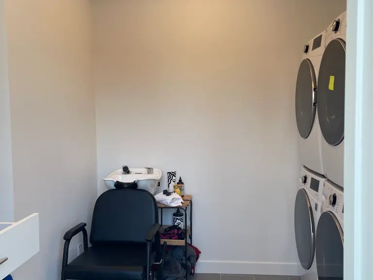 Laundry room after a dryer fire with plain white walls, a salon-style wash station in the corner, and stacked appliances on grey tile flooring