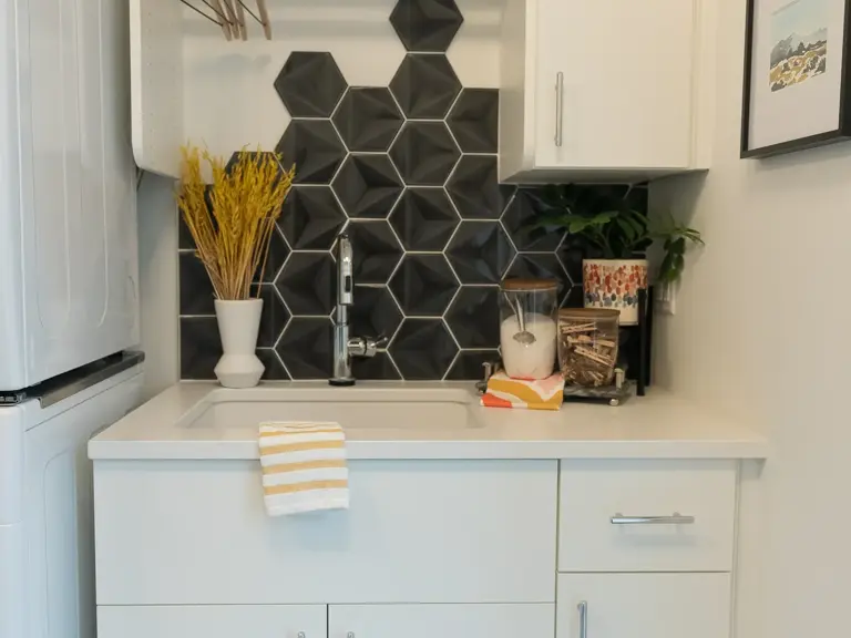 The same laundry sink after restoration with a black geometric-tile backsplash and open shelving on a hanging rod