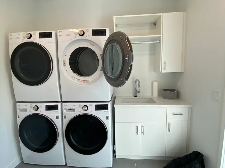 Laundry sink and folding counter below a plain white wall and an open hanging-rod cabinet before restoration