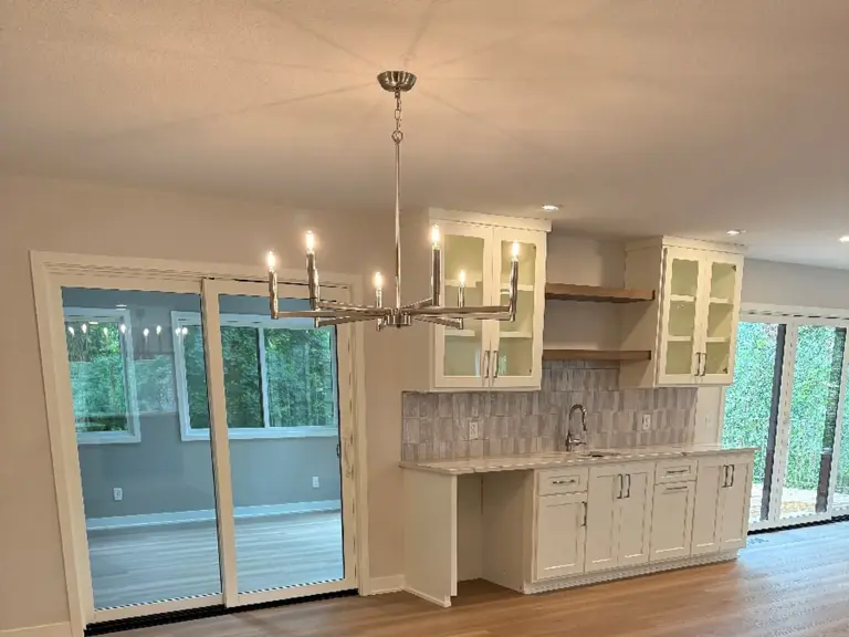 The same wall rebuilt with white cabinetry, glass-front uppers, and open shelving beside the patio door