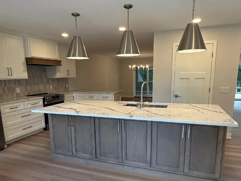 The peninsula replaced by a full island with a grey base, quartz top, and pendant lighting after restoration
