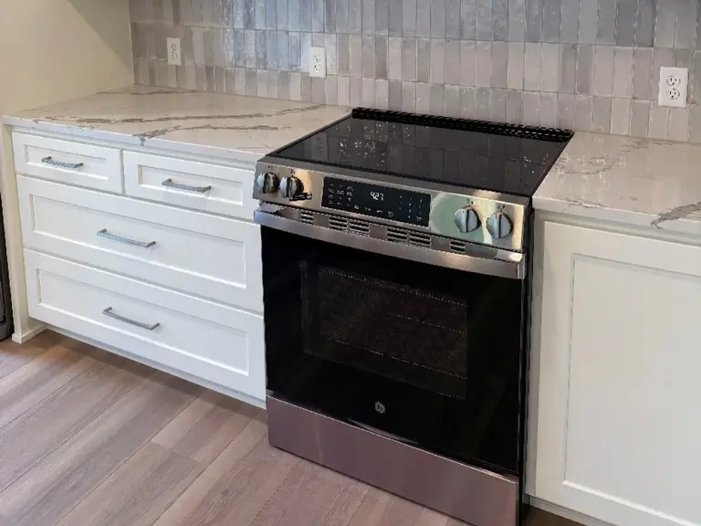 The same range wall rebuilt with a wood hood, white cabinetry, quartz counters, and grey tile backsplash