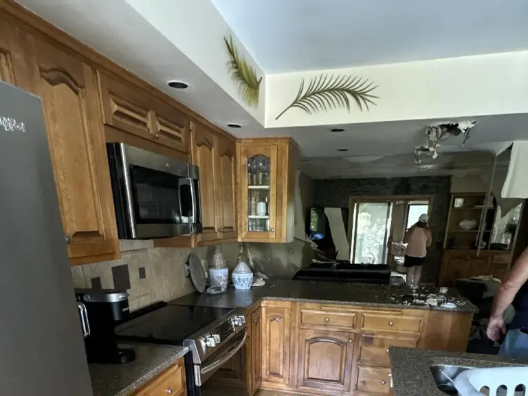 Original range wall with an over-range microwave, wood cabinets, and dark granite before fire restoration