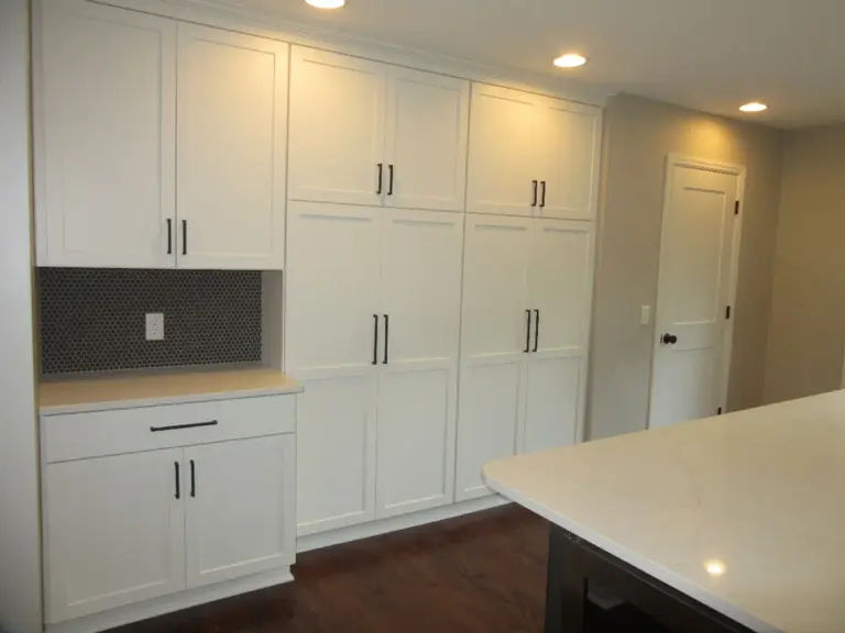 The same wall rebuilt as white floor-to-ceiling cabinetry with a tiled niche and black hardware