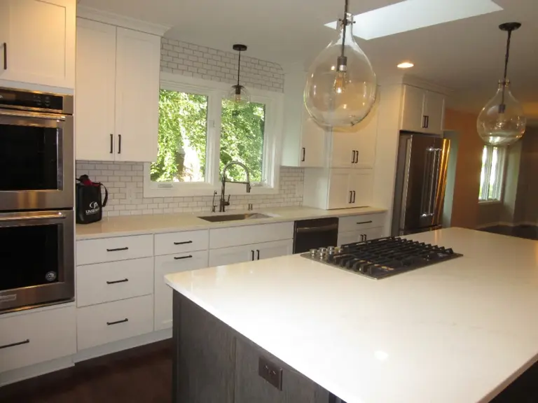 The same wall rebuilt with white cabinetry, quartz counters, subway tile, and stainless wall ovens