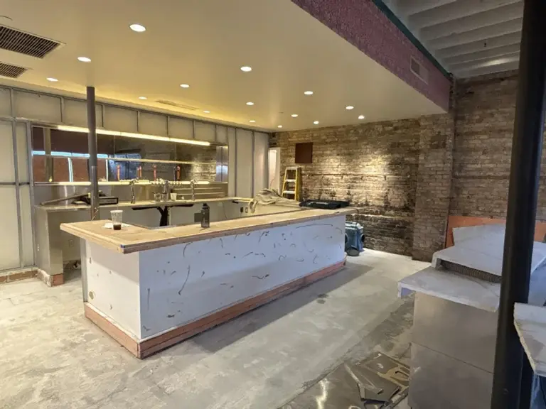 The old bar during demolition, with a stripped counter, bare concrete floor, and the building's original brick wall uncovered on the right