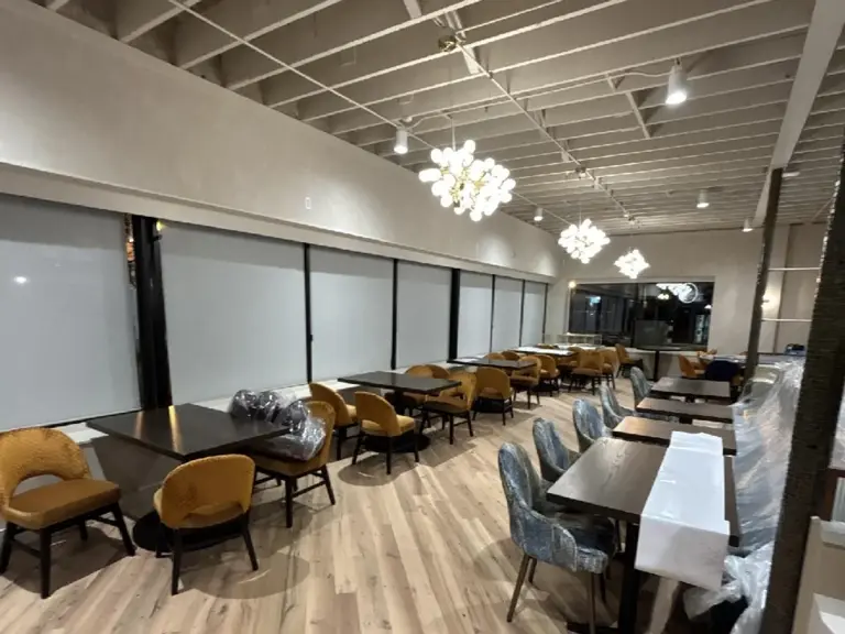The same dining room finished with wide-plank wood floors, reopened storefront glazing, painted exposed joists, and globe chandeliers