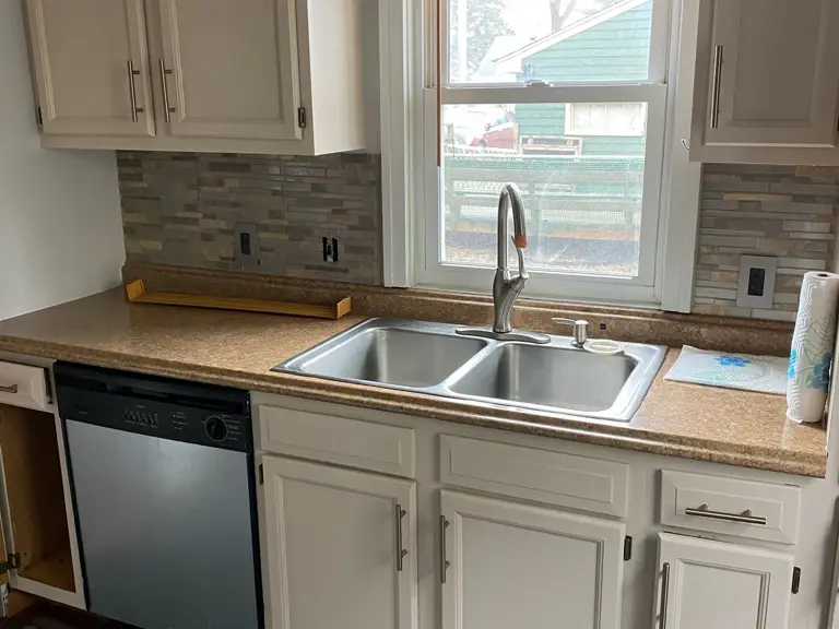 Dated kitchen with cream cabinets, laminate counters, and mosaic backsplash before restoration and renovation