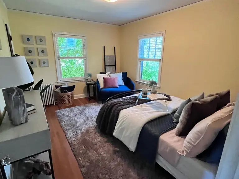 The same bedroom staged after restoration, with refinished hardwood floors and the radiator restored beneath the window