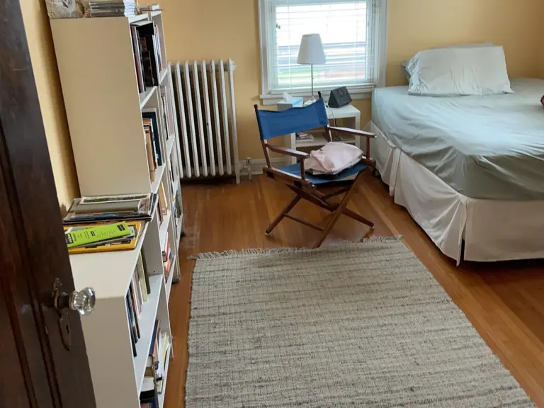 Yellow bedroom with a white column radiator under the window and worn hardwood floors before restoration
