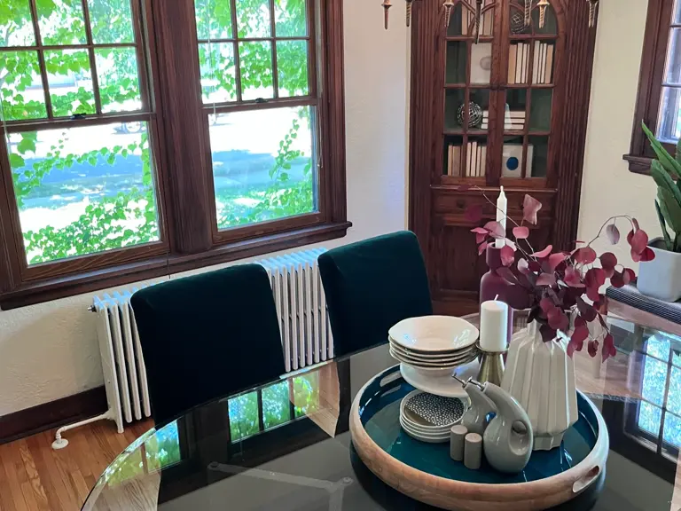 The same dining corner after restoration, with refinished hardwood floors, a clean column radiator under the windows, and the built-in cabinet intact