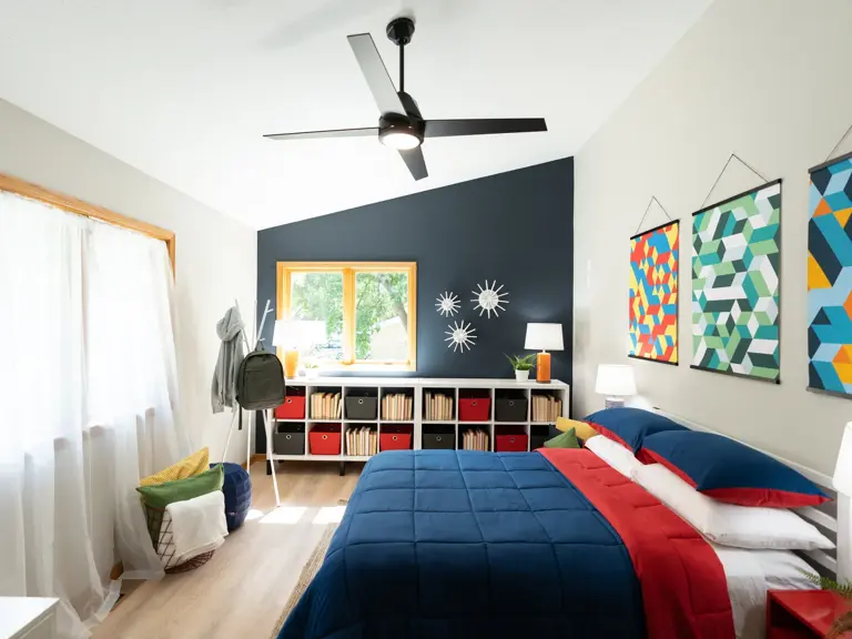 Restored upstairs bedroom with a raised vaulted ceiling, navy accent wall, and cube storage beneath the same window