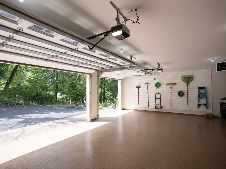 Rebuilt garage with white shiplap walls, a wall-mounted tool storage system, and a sealed flake floor after fire restoration