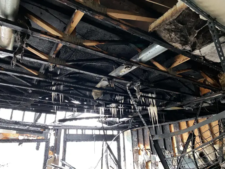 Garage gutted by fire, with charred roof framing and burned-out overhead door openings after a propane heater fire