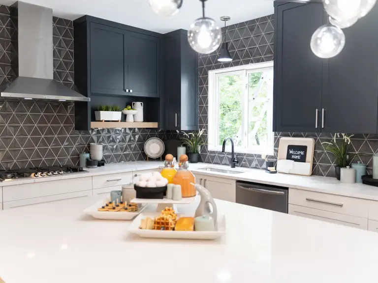 Rebuilt kitchen with navy cabinets, a white quartz island, faceted grey tile backsplash, and stainless range hood